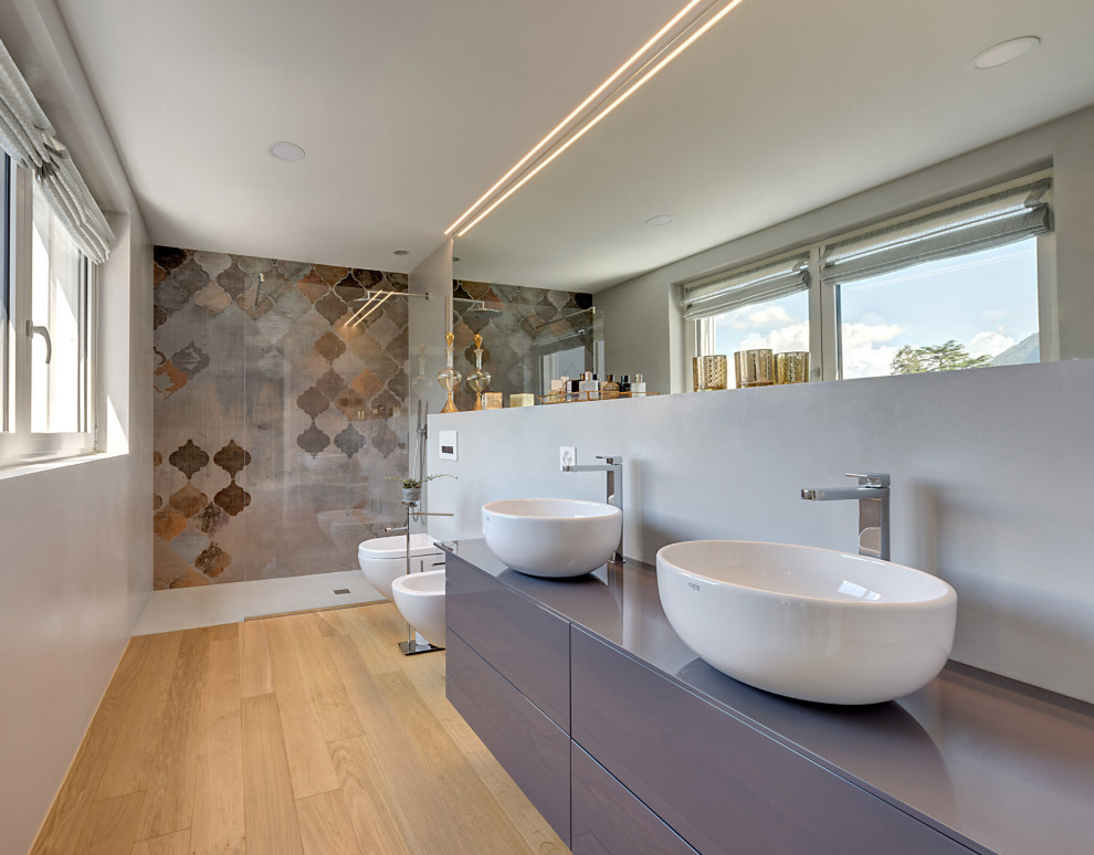 Bild på ett funkis grå grått en-suite badrum, med släta luckor, grå skåp, en kantlös dusch, en vägghängd toalettstol, grå väggar, mellanmörkt trägolv och ett fristående handfat