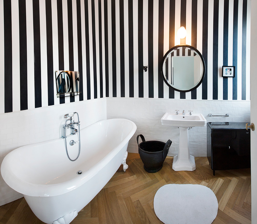Klassisk inredning av ett badrum, med ett piedestal handfat, flerfärgade väggar, ljust trägolv och ett badkar med tassar