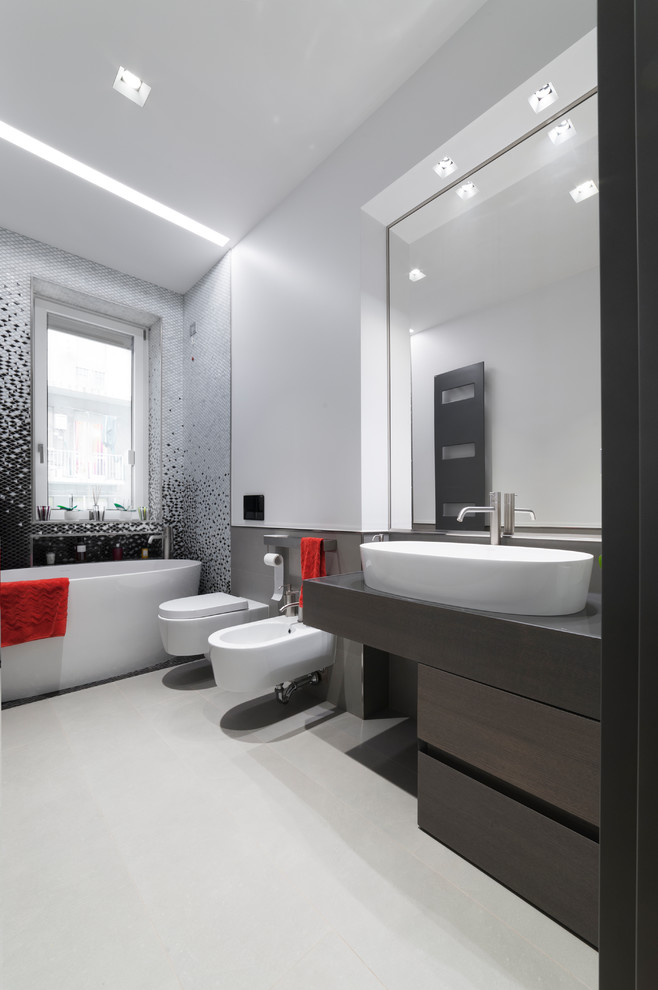 Design ideas for a medium sized modern ensuite bathroom in Milan with flat-panel cabinets, grey cabinets, a freestanding bath, a two-piece toilet, grey tiles, porcelain tiles, white walls, porcelain flooring, a vessel sink, glass worktops and grey floors.