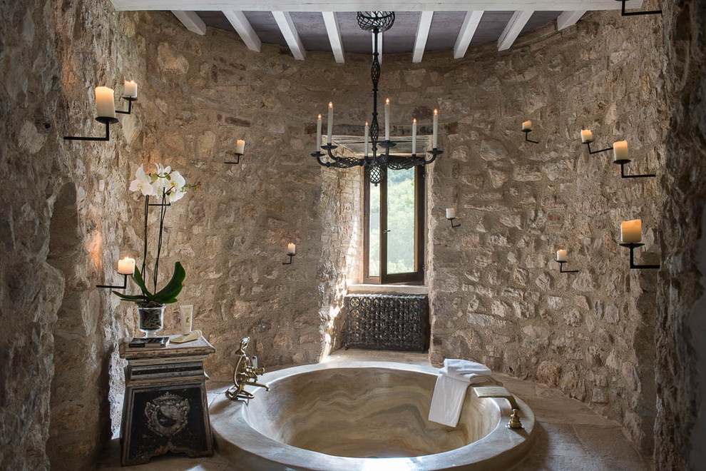 Immagine di una stanza da bagno mediterranea con vasca da incasso, pareti beige e pavimento in pietra calcarea