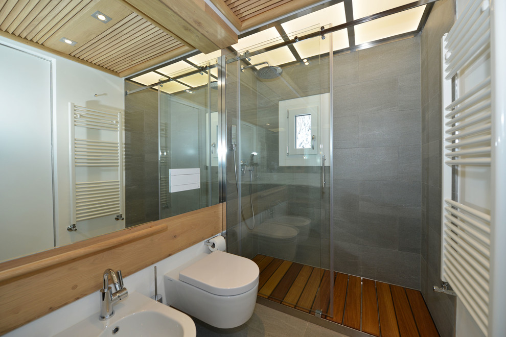 Inredning av ett rustikt litet badrum med dusch, med skåp i ljust trä, en kantlös dusch, en vägghängd toalettstol, grå kakel, stenkakel, vita väggar, klinkergolv i porslin, grått golv och dusch med skjutdörr