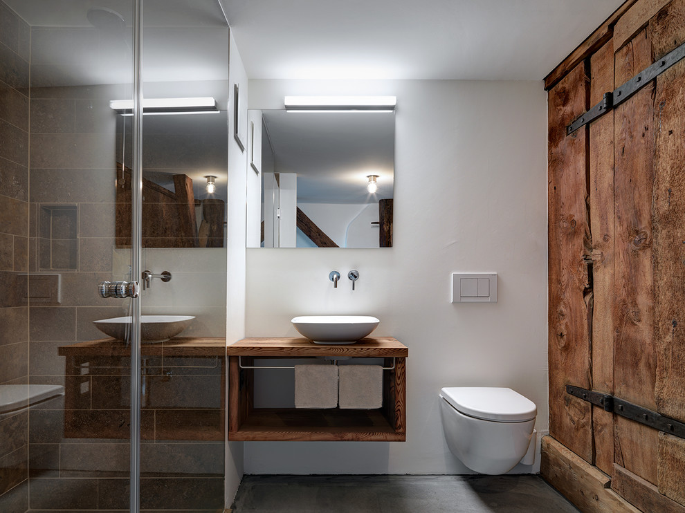 Cette photo montre une salle d'eau montagne en bois brun de taille moyenne avec un placard sans porte, WC suspendus, un mur blanc, sol en béton ciré, une vasque, un plan de toilette en bois, un sol gris et un plan de toilette marron.