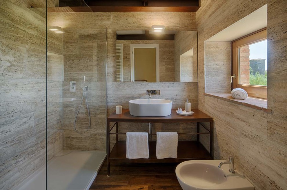 Foto på ett funkis brun badrum, med öppna hyllor, skåp i mörkt trä, en bidé, ett fristående handfat, en hörndusch, beige kakel, beige väggar, mellanmörkt trägolv, brunt golv och med dusch som är öppen