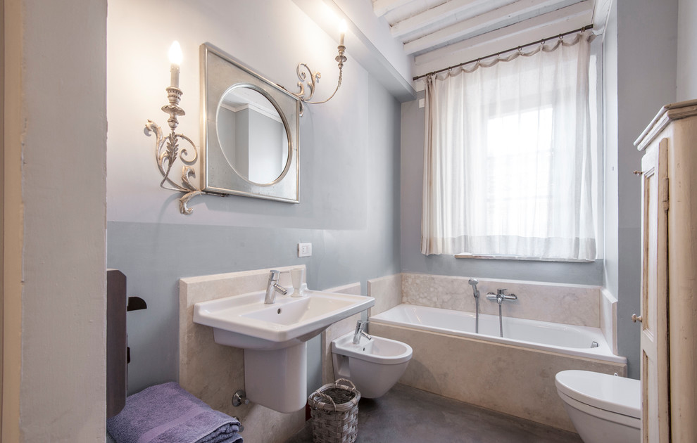 Ispirazione per una stanza da bagno padronale mediterranea di medie dimensioni con vasca/doccia, bidè, pareti blu, pavimento grigio, vasca da incasso, pavimento in cemento e lavabo sospeso