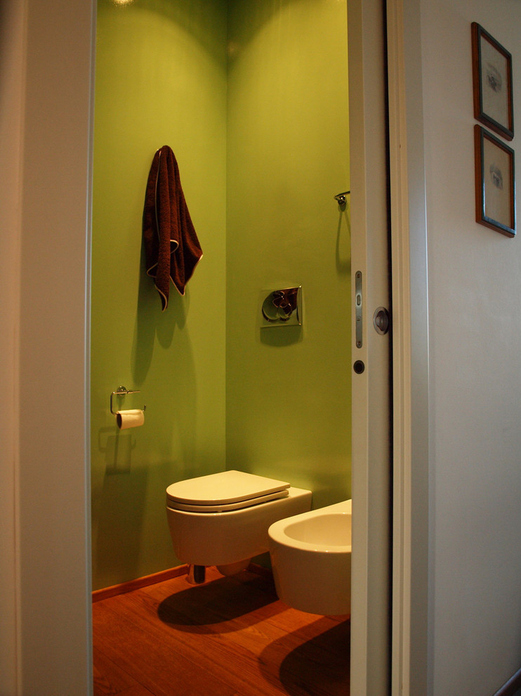 Kleines Modernes Duschbad mit flächenbündigen Schrankfronten, dunklen Holzschränken, Duschnische, Wandtoilette mit Spülkasten, grüner Wandfarbe, braunem Holzboden, Aufsatzwaschbecken und Waschtisch aus Holz in Mailand
