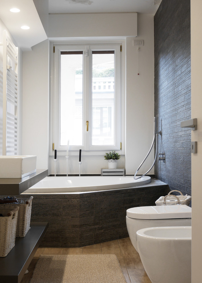 Foto på ett mellanstort funkis grå badrum, med öppna hyllor, grå skåp, ett platsbyggt badkar, en dusch/badkar-kombination, en bidé, grå kakel, vita väggar, ljust trägolv, ett fristående handfat, beiget golv och med dusch som är öppen