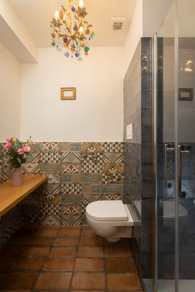 Idéer för att renovera ett mellanstort funkis beige beige badrum med dusch, med en dusch i en alkov, en vägghängd toalettstol, flerfärgad kakel, mosaik, vita väggar, klinkergolv i terrakotta, brunt golv och dusch med gångjärnsdörr