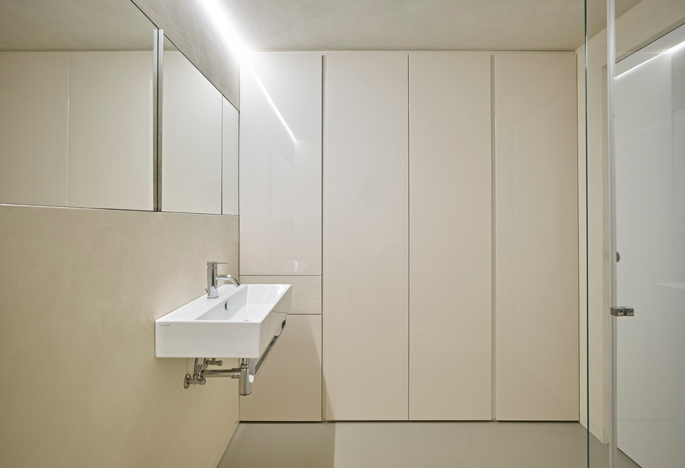 Bild på ett funkis badrum med dusch, med en vägghängd toalettstol, ett väggmonterat handfat, släta luckor, beige skåp, ett platsbyggt badkar, en kantlös dusch och beige väggar