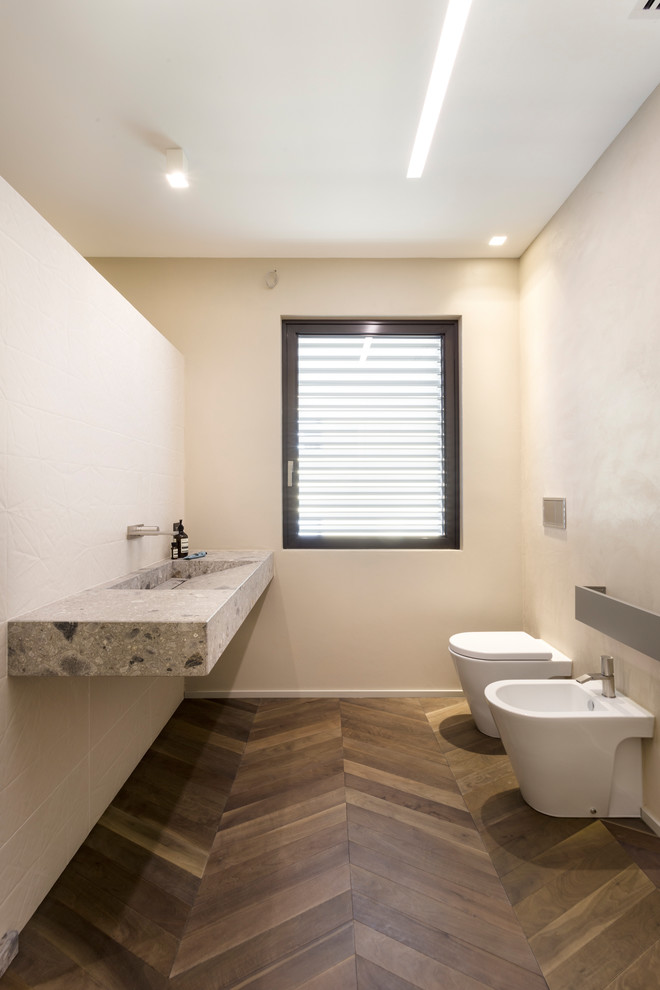 Diseño de cuarto de baño contemporáneo con urinario, paredes beige, suelo de madera en tonos medios, lavabo integrado, suelo marrón y encimeras grises