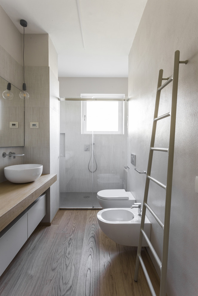 Inredning av ett modernt mellanstort beige beige badrum med dusch, med släta luckor, vita skåp, en dusch i en alkov, en bidé, ett fristående handfat, träbänkskiva, dusch med gångjärnsdörr, vit kakel och ljust trägolv