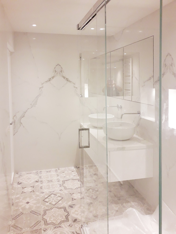 Inredning av ett modernt litet vit vitt badrum med dusch, med vita skåp, en kantlös dusch, en toalettstol med separat cisternkåpa, flerfärgad kakel, porslinskakel, vita väggar, cementgolv, ett fristående handfat, marmorbänkskiva, flerfärgat golv och dusch med skjutdörr