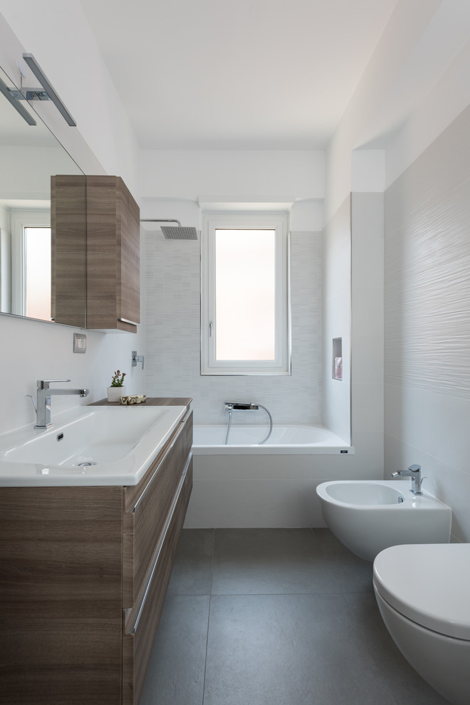 Bild på ett funkis badrum, med skåp i mörkt trä, ett platsbyggt badkar, en dusch/badkar-kombination, en toalettstol med separat cisternkåpa, ett nedsänkt handfat och grått golv