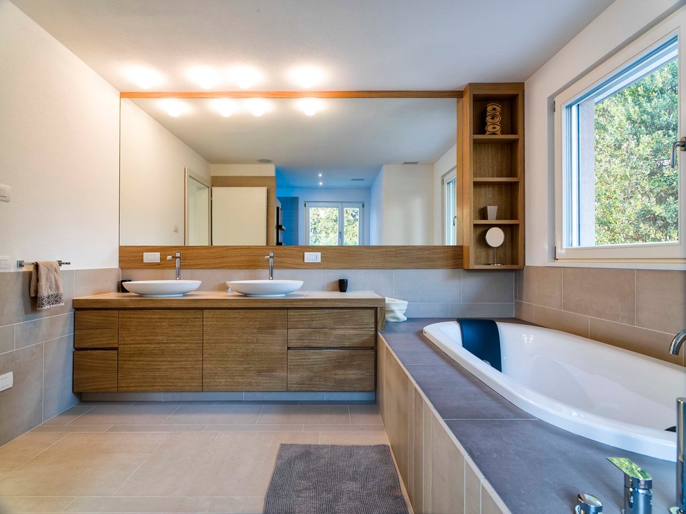 Imagen de cuarto de baño actual con lavabo sobreencimera, armarios con paneles lisos, puertas de armario de madera oscura, bañera encastrada, paredes blancas y ventanas