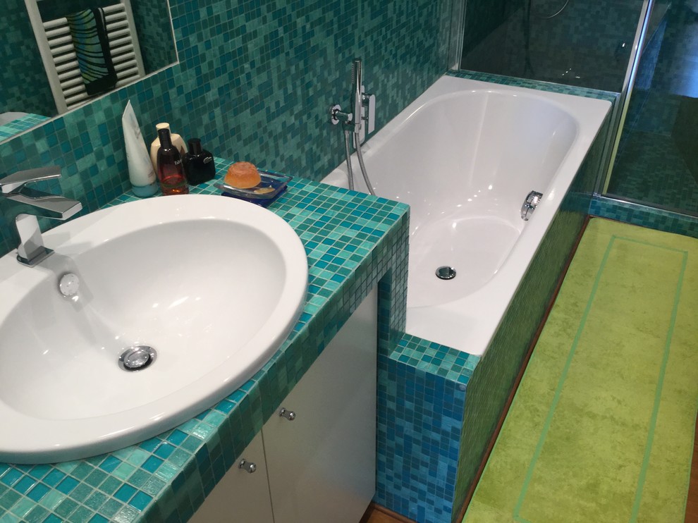 Modern inredning av ett stort grön grönt badrum med dusch, med öppna hyllor, vita skåp, ett platsbyggt badkar, grön kakel, mosaik, vita väggar, ljust trägolv, ett nedsänkt handfat, kaklad bänkskiva och dusch med gångjärnsdörr