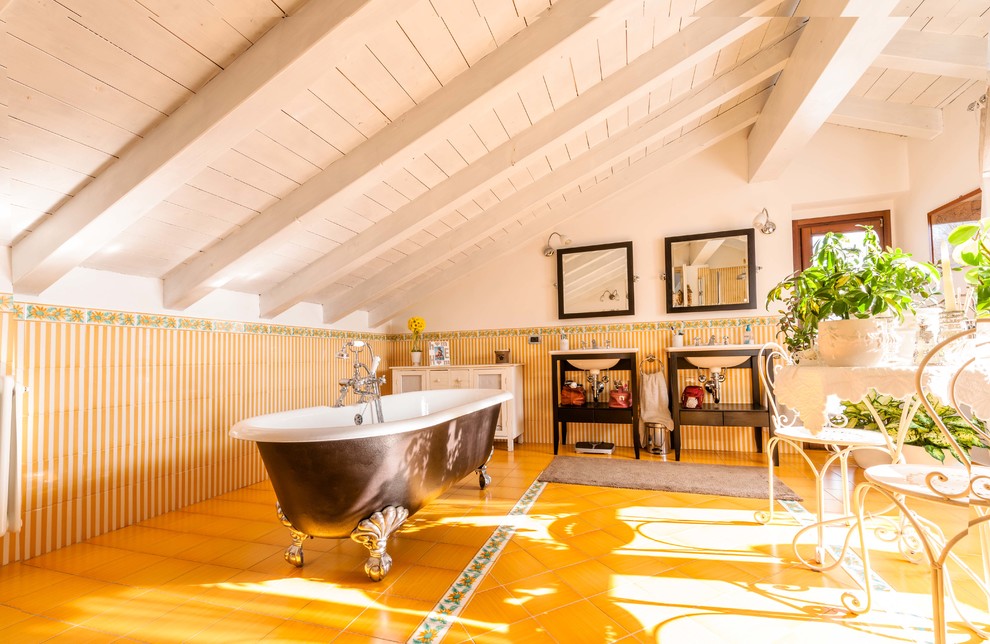 Inredning av ett lantligt badrum, med ett konsol handfat, skåp i mörkt trä, ett badkar med tassar, gul kakel och gula väggar