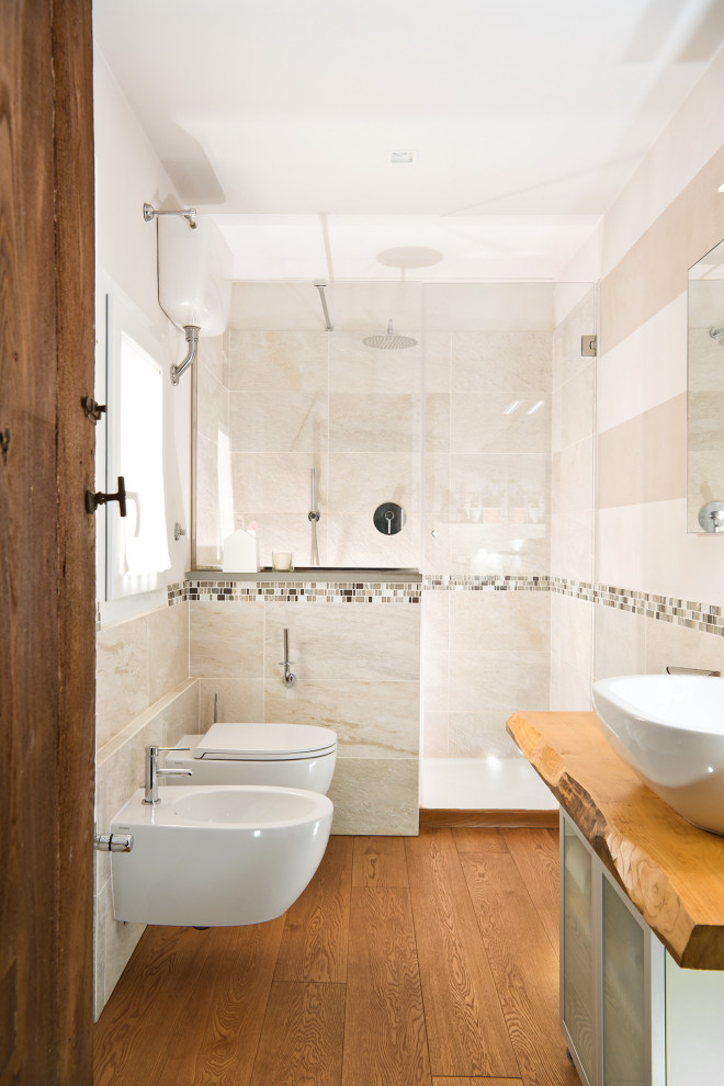 Idéer för ett litet medelhavsstil brun badrum med dusch, med luckor med glaspanel, vita skåp, en vägghängd toalettstol, beige kakel, keramikplattor, vita väggar, ett fristående handfat, brunt golv, en dusch i en alkov, mellanmörkt trägolv och träbänkskiva