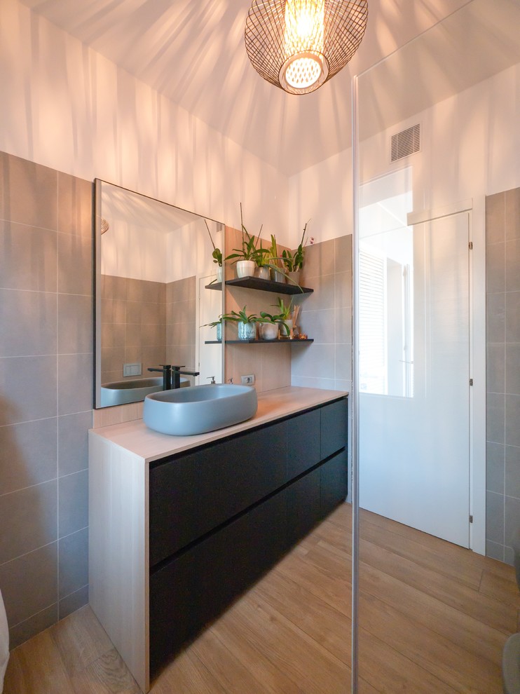 Example of a mid-sized danish 3/4 gray tile and porcelain tile porcelain tile and beige floor corner shower design in Milan with flat-panel cabinets, black cabinets, a wall-mount toilet, white walls, a vessel sink, wood countertops and a hinged shower door