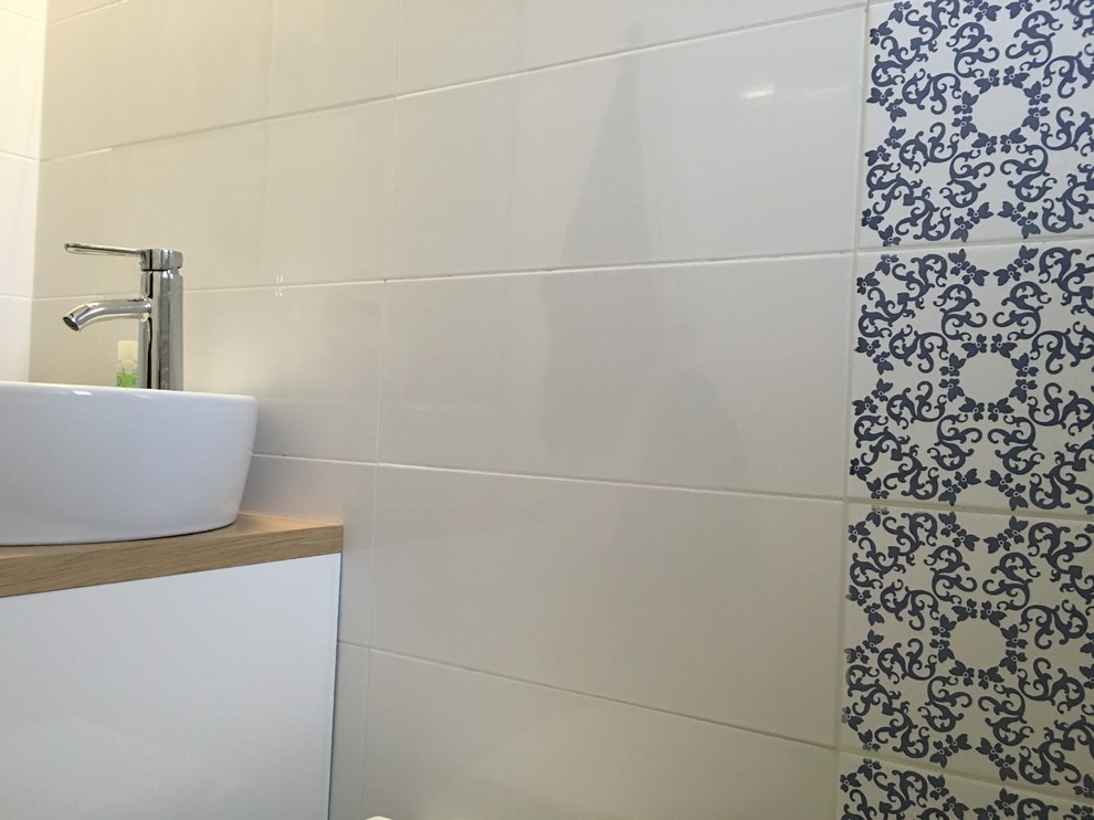 Inredning av ett medelhavsstil litet badrum med dusch, med luckor med profilerade fronter, vita skåp, en kantlös dusch, en toalettstol med hel cisternkåpa, vit kakel, keramikplattor, blå väggar, ett fristående handfat, brunt golv och med dusch som är öppen