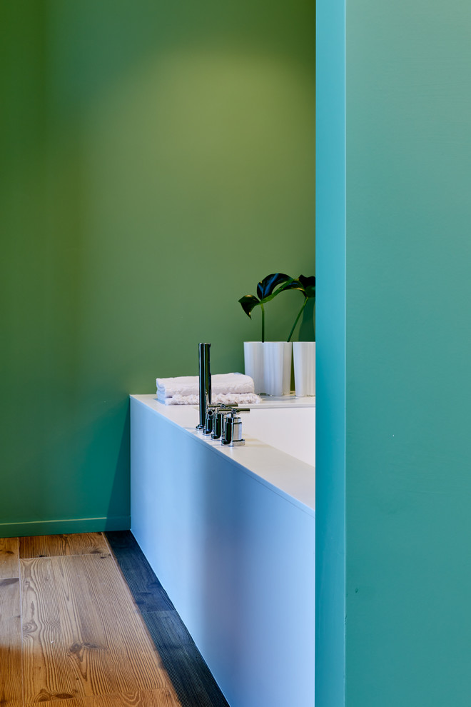 Immagine di una stanza da bagno minimalista con nessun'anta, pareti verdi, lavabo integrato, pavimento marrone e top bianco