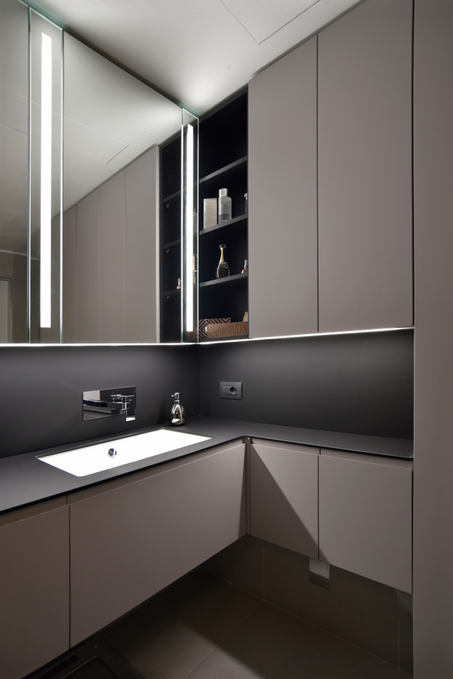 Immagine di una stanza da bagno minimal con ante lisce, ante grigie, lavabo sottopiano e top nero