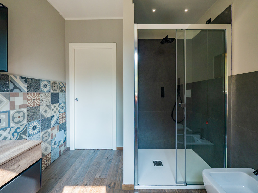 Medium sized contemporary shower room bathroom in Milan with flat-panel cabinets, dark wood cabinets, an alcove shower, a two-piece toilet, grey tiles, porcelain tiles, beige walls, dark hardwood flooring, a vessel sink, wooden worktops and a sliding door.