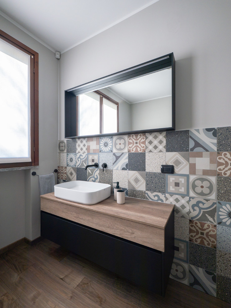 Bild på ett mellanstort funkis brun brunt badrum med dusch, med släta luckor, skåp i mörkt trä, porslinskakel, mörkt trägolv, ett fristående handfat, träbänkskiva, flerfärgad kakel, grå väggar och brunt golv