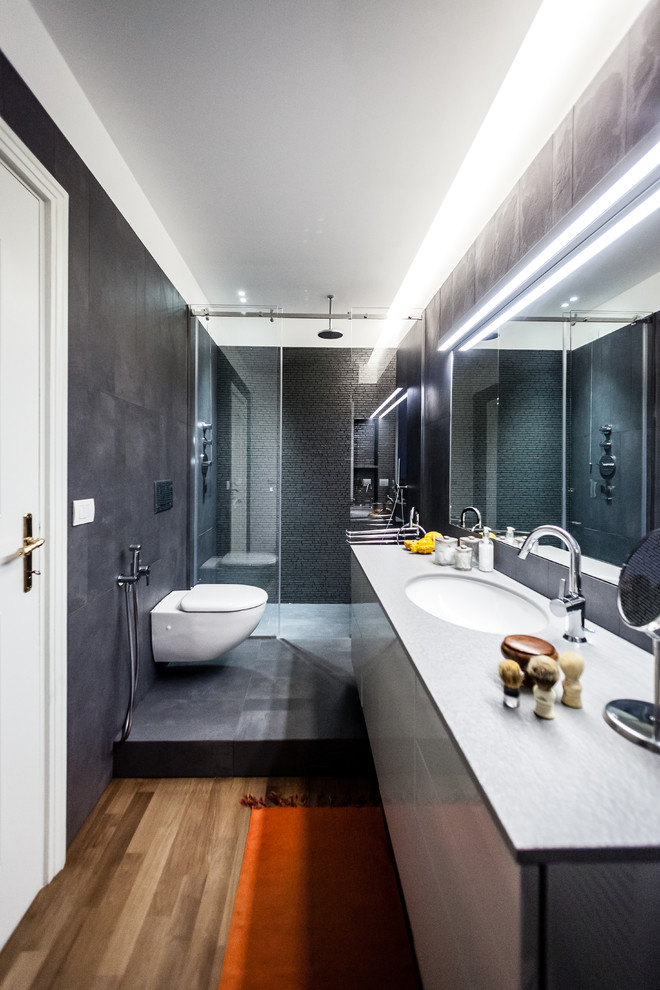 Small contemporary shower room bathroom in Milan with flat-panel cabinets, a corner shower, grey tiles, black tiles, grey walls, medium hardwood flooring, an integrated sink, marble worktops and a sliding door.