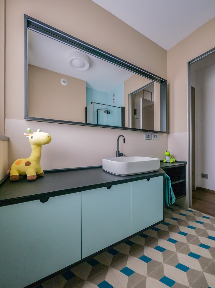 Foto på ett litet funkis svart badrum för barn, med släta luckor, beige kakel, porslinskakel, beige väggar, cementgolv, ett fristående handfat, bänkskiva i akrylsten, flerfärgat golv och blå skåp