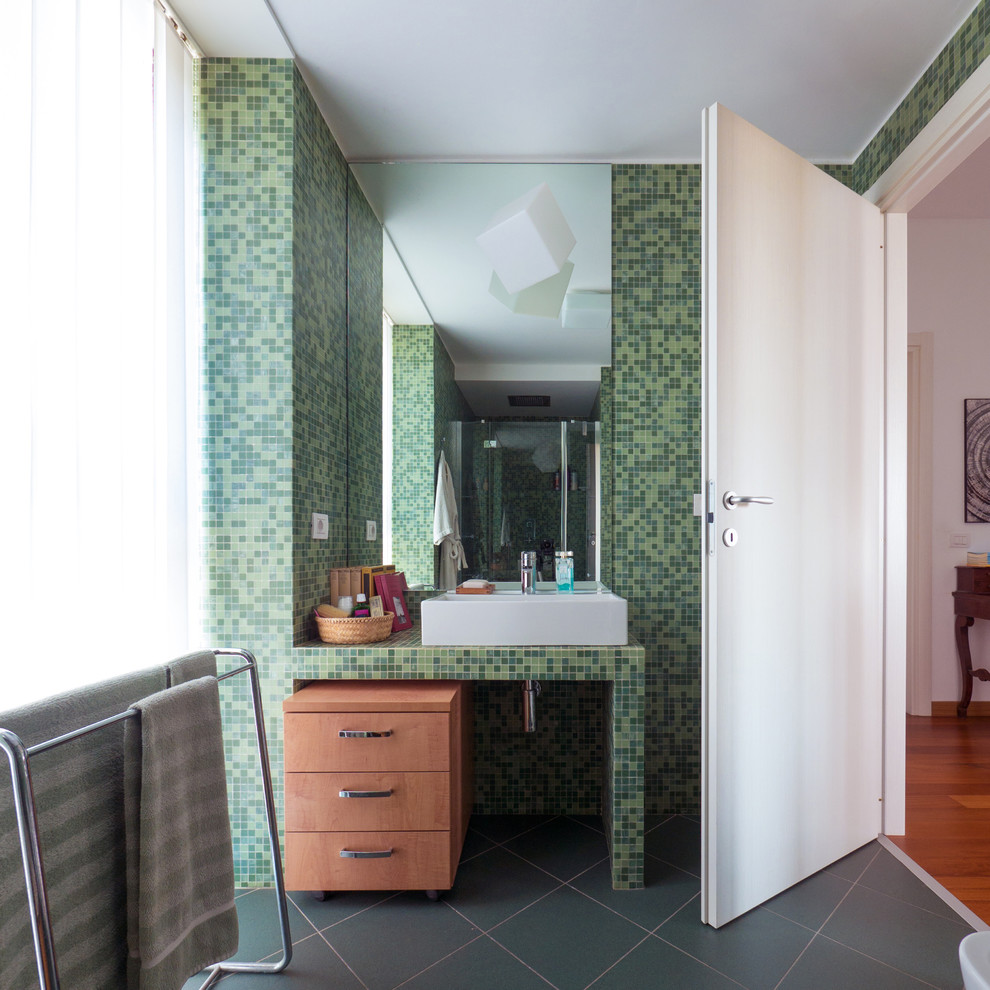 Kleines Modernes Badezimmer En Suite mit flächenbündigen Schrankfronten, hellen Holzschränken, Duschnische, Wandtoilette mit Spülkasten, grünen Fliesen, Mosaikfliesen, grüner Wandfarbe, Keramikboden, Trogwaschbecken, gefliestem Waschtisch, grünem Boden, Falttür-Duschabtrennung und grüner Waschtischplatte in Mailand
