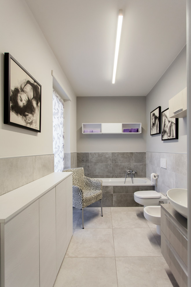 Foto på ett mellanstort funkis badrum, med släta luckor, grå skåp, en vägghängd toalettstol, grå kakel, porslinskakel, grå väggar, klinkergolv i porslin, ett fristående handfat och laminatbänkskiva