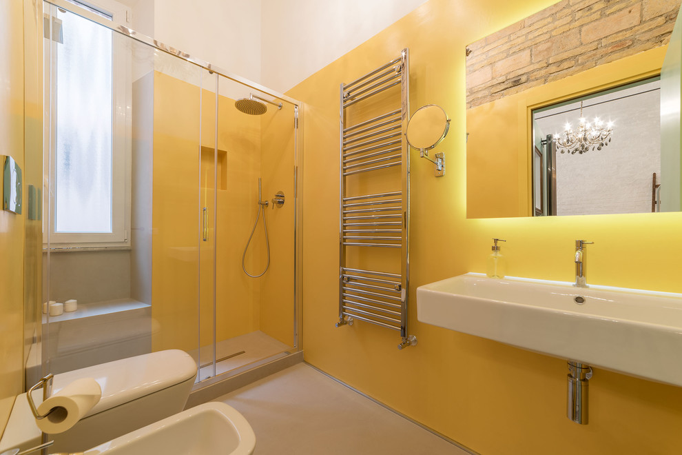 Immagine di una stanza da bagno con doccia eclettica con doccia alcova, WC sospeso, pareti gialle, pavimento in cemento, lavabo sospeso, pavimento beige e porta doccia scorrevole