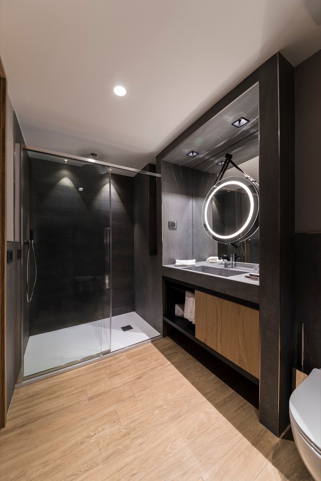 Cette image montre une salle de bain design en bois clair avec un placard à porte plane, un mur noir, parquet clair, un lavabo intégré et un plan de toilette en béton.
