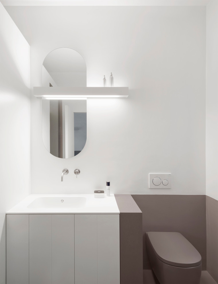 Cette photo montre une petite salle de bain moderne avec un placard à porte plane, des portes de placard grises, WC suspendus, un mur gris, un lavabo posé, un plan de toilette en surface solide, un sol gris, une cabine de douche à porte battante et un plan de toilette blanc.
