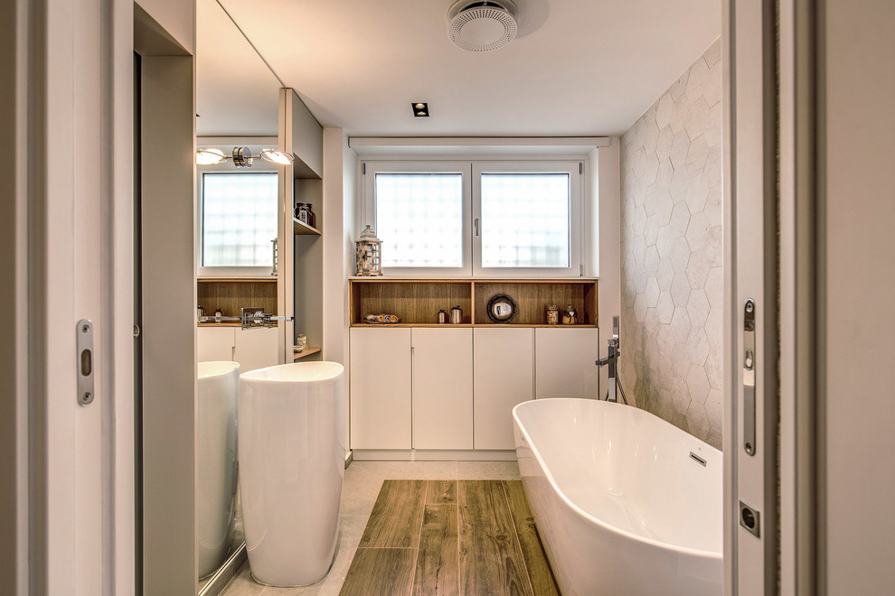 Идея дизайна: главная ванная комната в современном стиле с плоскими фасадами, белыми фасадами, отдельно стоящей ванной, серой плиткой, серыми стенами, темным паркетным полом, консольной раковиной и коричневым полом
