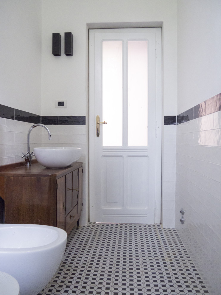 50 tals inredning av ett litet brun brunt badrum med dusch, med möbel-liknande, skåp i mörkt trä, en dusch i en alkov, en vägghängd toalettstol, vit kakel, keramikplattor, vita väggar, klinkergolv i porslin, ett fristående handfat, träbänkskiva och svart golv