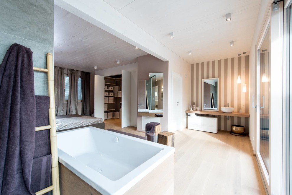 Exempel på ett mycket stort modernt en-suite badrum, med släta luckor, vita skåp, ett fristående badkar, flerfärgade väggar, ljust trägolv och träbänkskiva