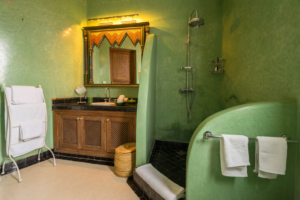Ejemplo de cuarto de baño mediterráneo con paredes verdes, aseo y ducha, ducha abierta, armarios con paneles empotrados, puertas de armario de madera oscura, ducha esquinera, lavabo encastrado, suelo beige y encimeras negras