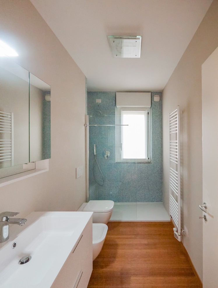 Пример оригинального дизайна: ванная комната среднего размера в современном стиле с плоскими фасадами, белыми фасадами, душем в нише, инсталляцией, синей плиткой, стеклянной плиткой, бежевыми стенами, полом из бамбука, душевой кабиной, консольной раковиной, столешницей из искусственного камня, душем с распашными дверями и белой столешницей