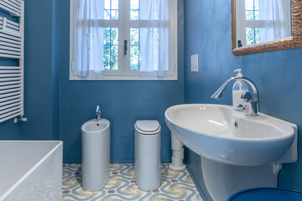 Foto på ett litet industriellt en-suite badrum, med ett fristående badkar, en toalettstol med separat cisternkåpa, blå väggar, marmorgolv, ett väggmonterat handfat och flerfärgat golv