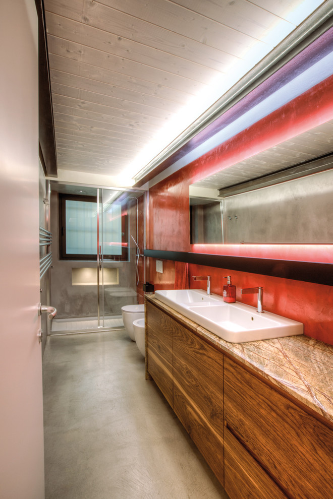 Cette photo montre une salle de bain tendance en bois brun de taille moyenne avec un placard à porte plane, WC suspendus, un mur rouge, un lavabo posé, une cabine de douche à porte coulissante, sol en béton ciré, un sol gris et un plan de toilette marron.