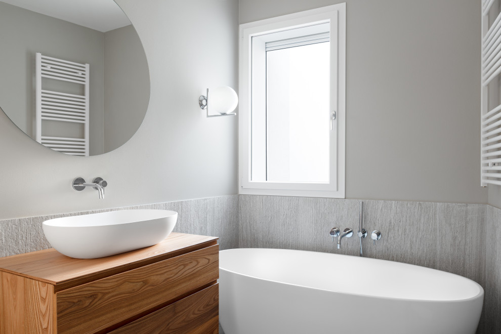 Example of a trendy 3/4 gray tile freestanding bathtub design in Venice with flat-panel cabinets, dark wood cabinets, gray walls, a vessel sink, wood countertops and brown countertops