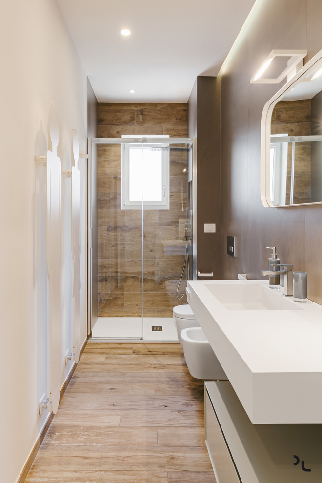 Cette image montre une salle de bain principale minimaliste de taille moyenne avec un placard à porte plane, des portes de placards vertess, WC suspendus, un carrelage marron, des dalles de pierre, un mur blanc, un sol en carrelage de porcelaine, un plan de toilette en surface solide, une cabine de douche à porte battante, un plan de toilette blanc, un lavabo intégré, une douche à l'italienne, un sol beige et meuble simple vasque.
