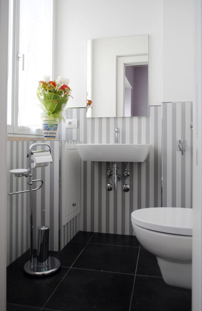 Foto de cuarto de baño moderno con ducha a ras de suelo, sanitario de pared, baldosas y/o azulejos grises, baldosas y/o azulejos de porcelana, paredes blancas, suelo de baldosas de porcelana, aseo y ducha, lavabo suspendido, suelo negro y ducha abierta
