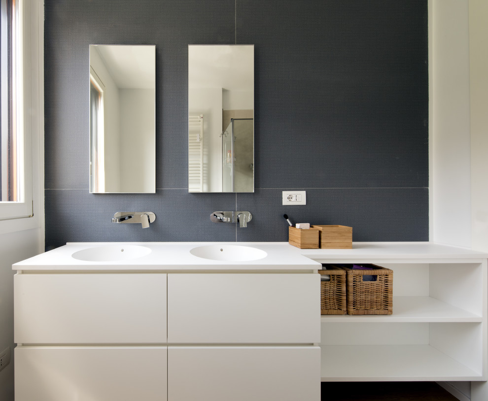 Mid-sized trendy master blue tile and porcelain tile light wood floor and beige floor corner shower photo in Milan with flat-panel cabinets, white cabinets, a two-piece toilet, white walls, an integrated sink, solid surface countertops and a hinged shower door