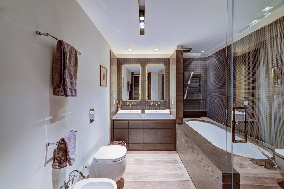 На фото: большая главная ванная комната в современном стиле с плоскими фасадами, инсталляцией, коричневой плиткой, керамогранитной плиткой, бежевыми стенами, полом из керамогранита, коричневыми фасадами, полновстраиваемой ванной и настольной раковиной с