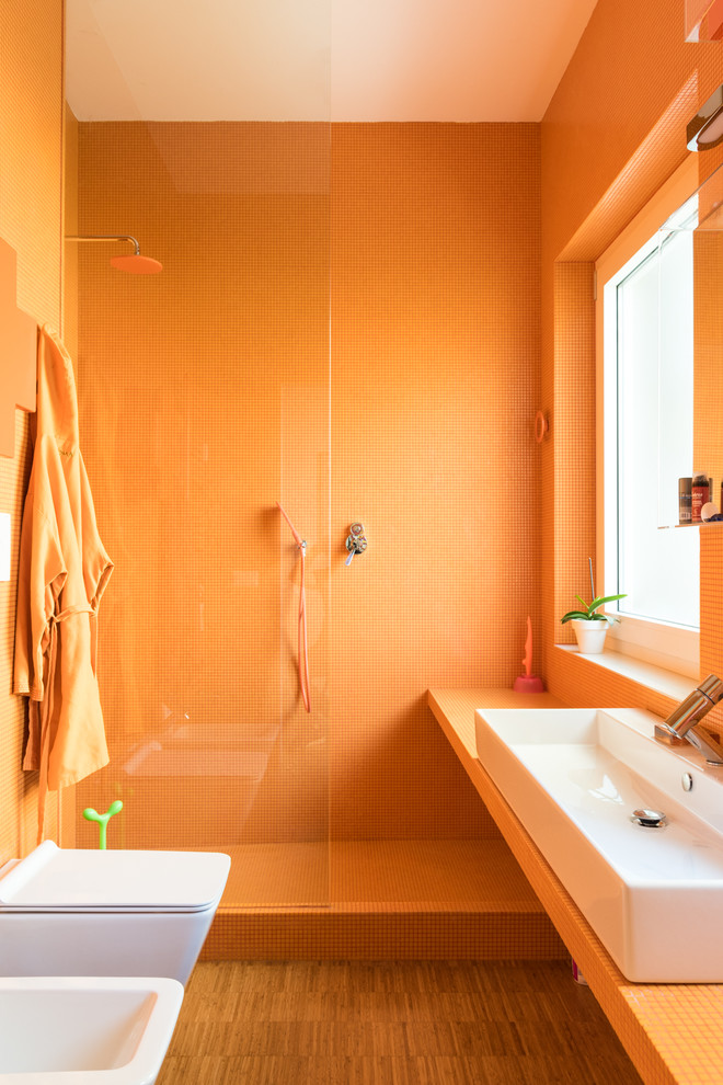 Stilmix Duschbad mit orangefarbenen Schränken, offener Dusche, Wandtoilette mit Spülkasten, orangen Fliesen, Mosaikfliesen, oranger Wandfarbe, hellem Holzboden, Aufsatzwaschbecken, gefliestem Waschtisch, offener Dusche und oranger Waschtischplatte in Rom