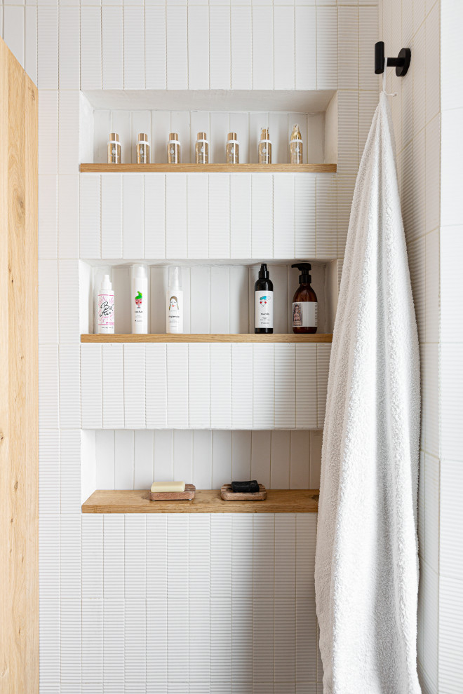 Bild på ett litet minimalistiskt badrum med dusch, med släta luckor, skåp i ljust trä, en kantlös dusch, en vägghängd toalettstol, vit kakel, stickkakel, vita väggar, betonggolv, ett fristående handfat, träbänkskiva, grått golv och med dusch som är öppen