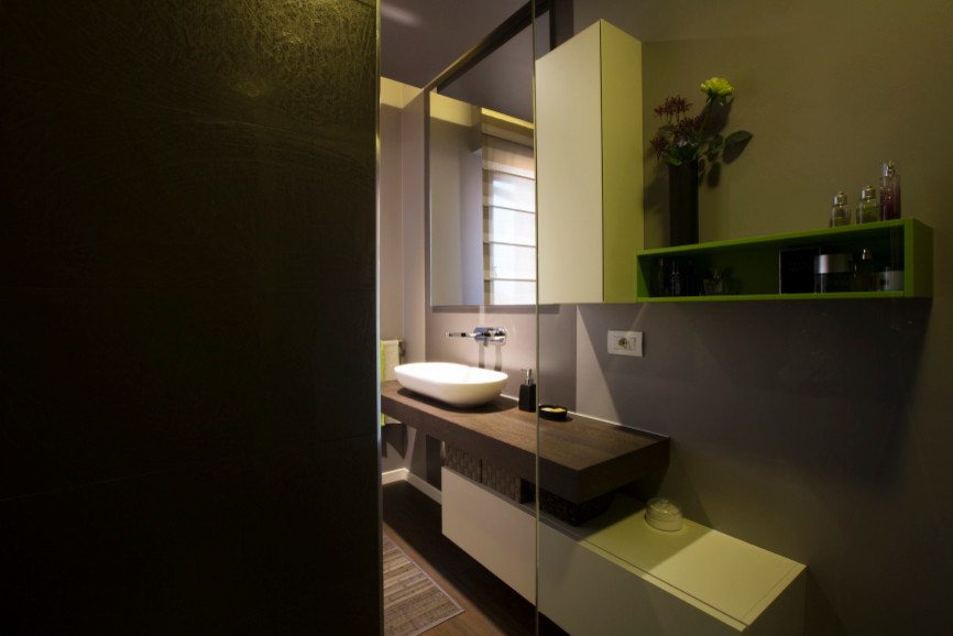 Inredning av ett modernt badrum med dusch, med släta luckor, vita skåp, en dubbeldusch, en toalettstol med separat cisternkåpa, svart kakel, porslinskakel, grå väggar, målat trägolv, ett fristående handfat, träbänkskiva och brunt golv