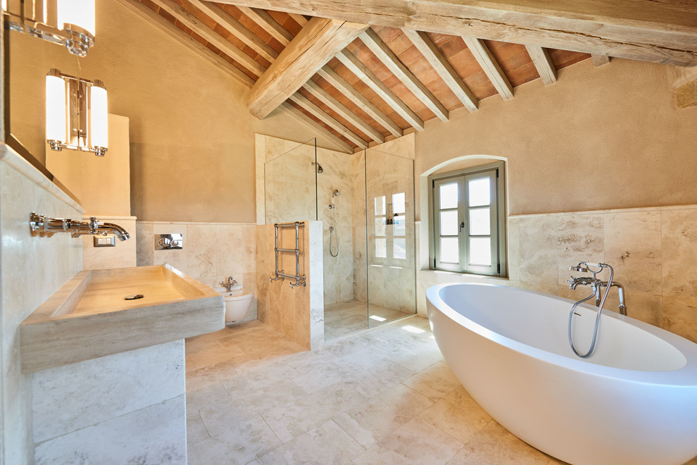 Medelhavsstil inredning av ett en-suite badrum, med ett fristående badkar, en kantlös dusch, en vägghängd toalettstol, beige kakel, beige väggar, ett avlångt handfat, beiget golv och med dusch som är öppen