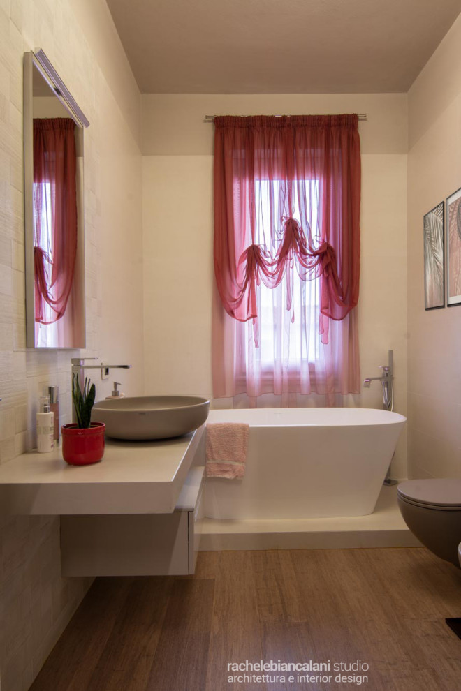 Cette image montre une très grande salle d'eau minimaliste avec un placard à porte plane, des portes de placard beiges, une baignoire indépendante, une douche d'angle, WC suspendus, un carrelage blanc, des carreaux de porcelaine, un mur beige, parquet en bambou, une vasque, un plan de toilette en granite, un sol marron, une cabine de douche à porte coulissante, un plan de toilette blanc, meuble simple vasque et meuble-lavabo suspendu.